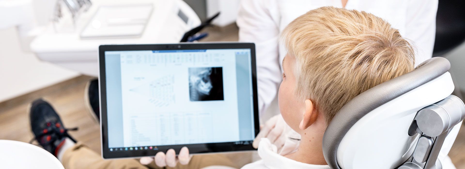 Kopfbild: Behandlungssituation, in der sich eine Junge ein Röntgenbild auf einem Tablet ansieht.