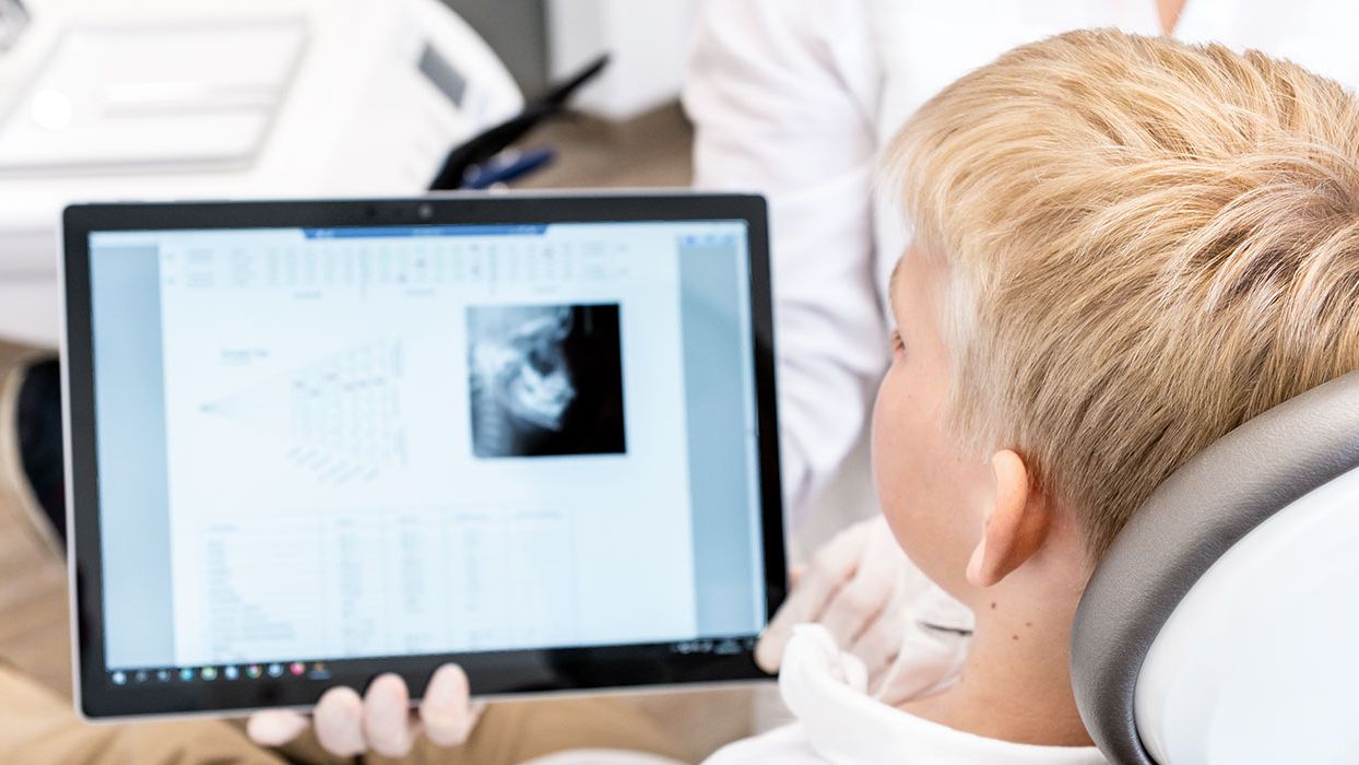 Kopfbild: Behandlungssituation, in der sich eine Junge ein Röntgenbild auf einem Tablet ansieht.